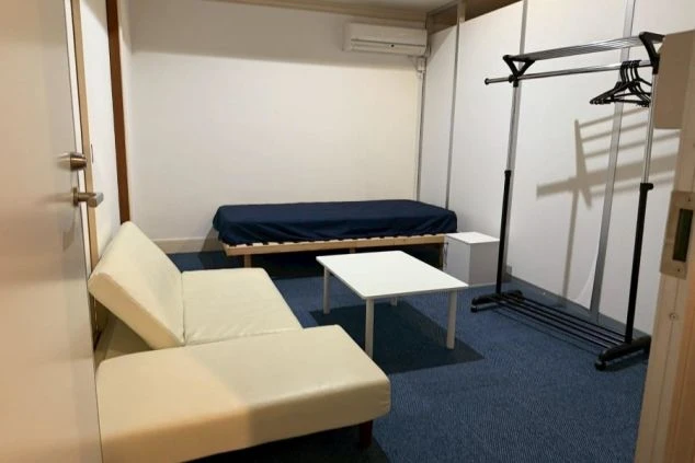 リゾートバイトの個室寮の部屋。ベッド、ソファ、テーブルが備え付けられた、広くてモダンな洋室。エアコンとハンガーラックも完備。