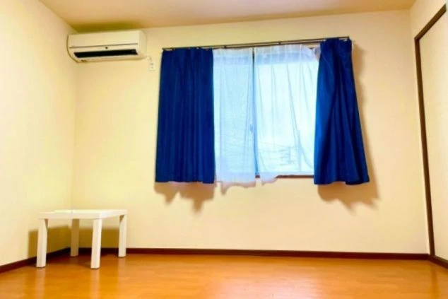 リゾートバイトの個室寮の室内。エアコンや小さなテーブルが備え付けられており、窓からは光が差し込む。快適な寮生活をアピールする画像。