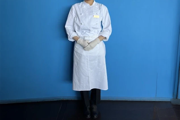 リゾートバイトの制服見本。白いコックコートとエプロン、手には手袋を着用。清潔感のある服装で、調理・調理補助の仕事をアピール。