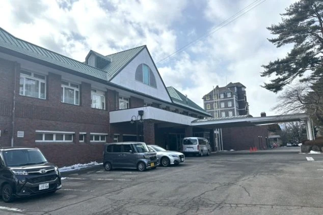 タイル張りの床に、テーブルと椅子が2つ置かれた明るいテラスの画像。大きな窓から光が差し込み、外の緑が見える。