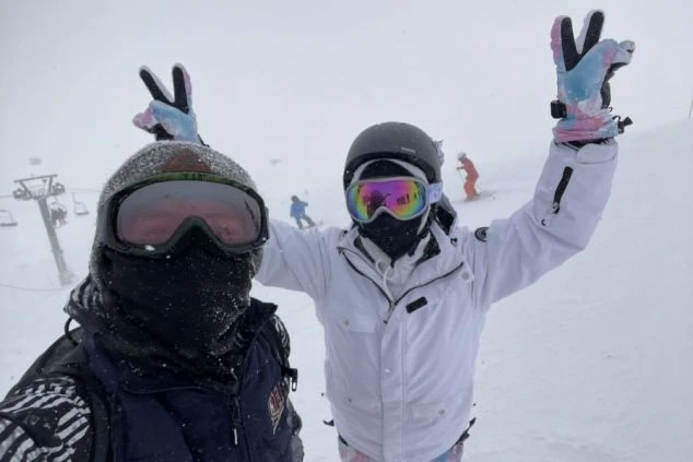 リゾートバイトの休日に仲間と楽しむイメージ画像。スキー場でスノーボードをしながら、楽しそうにポーズをとる2人。