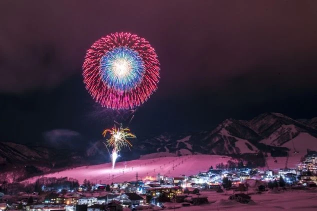 リゾートバイトの休日の観光イメージ画像。雪が積もった山とスキー場に、冬の夜空を彩る花火が打ち上げられている幻想的な風景。