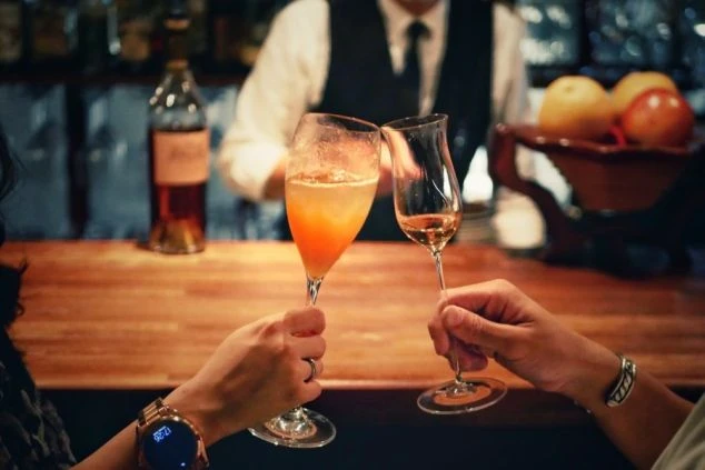 2人の男女が、バーカウンターでおしゃれなカクテルで乾杯している手元の画像。