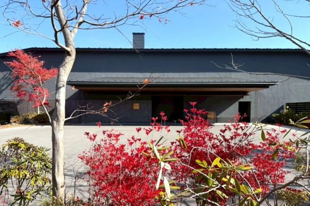 鮮やかな赤い紅葉に囲まれた、モダンでシックなデザインのホテルのエントランス。