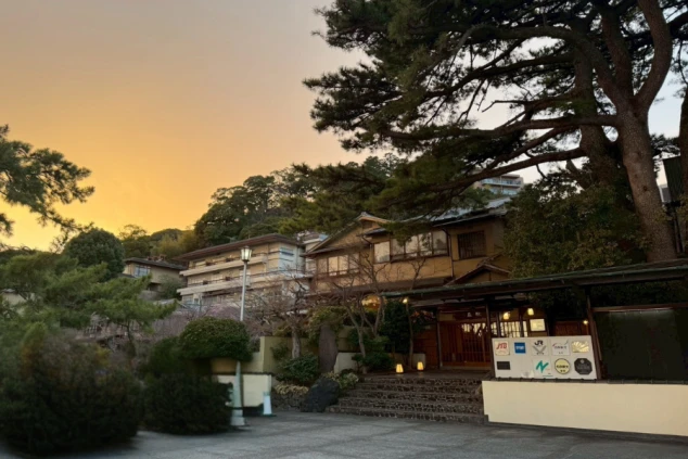 夕暮れ時の宿の玄関。松の巨木と趣ある和風建築。