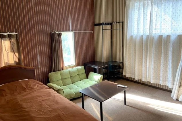 リゾートバイトの社員寮の部屋を表現するイメージ画像。ベッドやソファ、ハンガーラックが備え付けられたシンプルな個室。