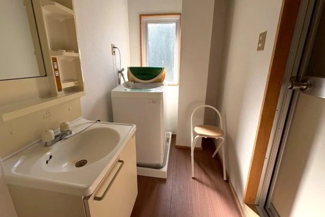 寮の共有スペースにある独立洗面台と洗濯機の画像。日常生活に必要な家電が揃っており、住み込み生活の利便性が高い。