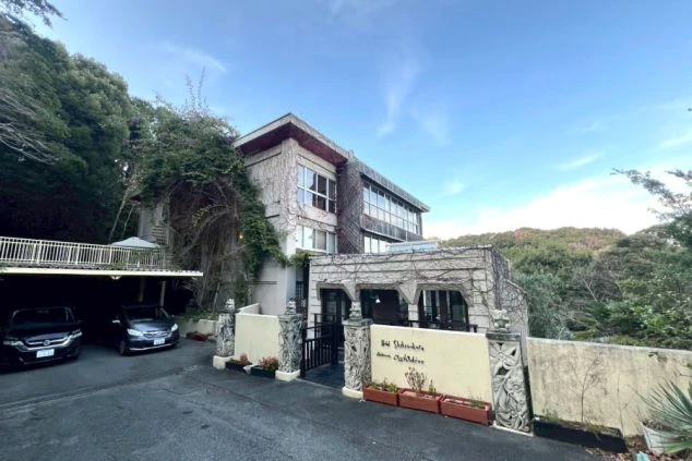 建物は蔦や緑の植物に覆われ、壁の下部には花やカエルをモチーフにした石像が置かれている。アジアンリゾートや隠れ家のような雰囲気がある。