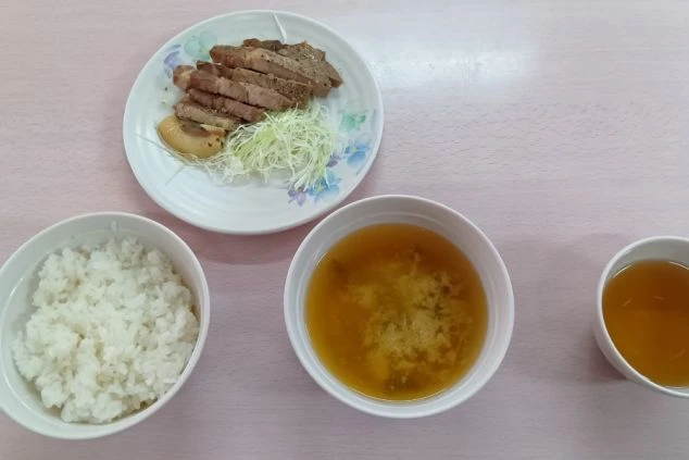メインの肉料理、ご飯、味噌汁、スープが写っている。