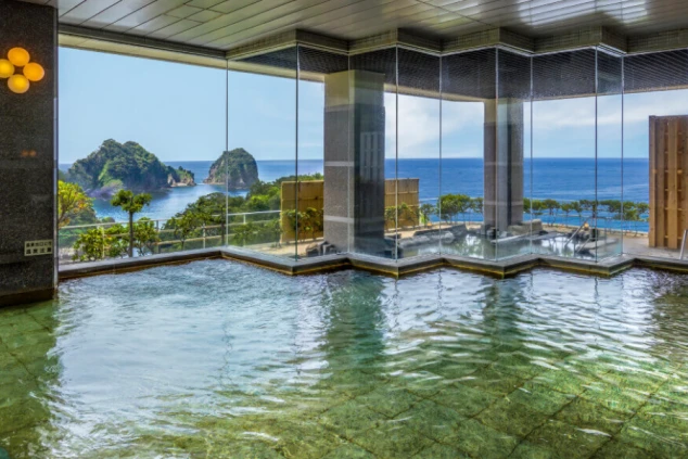 静岡県西伊豆にある堂ヶ島温泉のホテルの展望風呂。大きな窓から海と奇岩が一望できる。仕事の疲れを癒せる温泉や絶景を強調し、リゾートバイトの魅力を伝える。