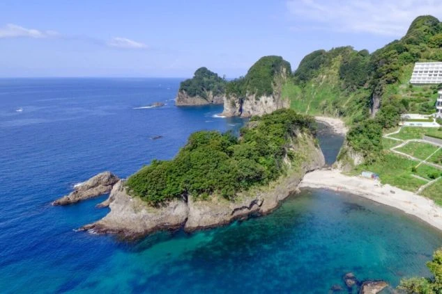 静岡県西伊豆にある堂ヶ島温泉の景観。青く澄んだ海に緑の木々が生い茂る奇岩が点在し、美しい海岸線を見下ろすホテルが写っている。リゾートバイトの勤務地として、非日常的な景色をアピール。