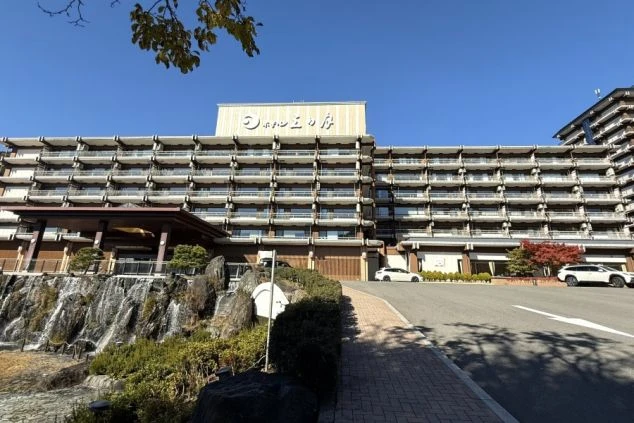 青空の下にそびえ立つ、滝のある庭園を備えた鬼怒川にあるホテルの外観の画像。