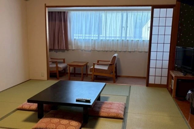 リゾートバイトの客室寮の和室の部屋の画像。黒い座卓と座布団が置かれ、窓際には椅子と小さなテーブルがある。リゾートバイトの寮の部屋の画像。