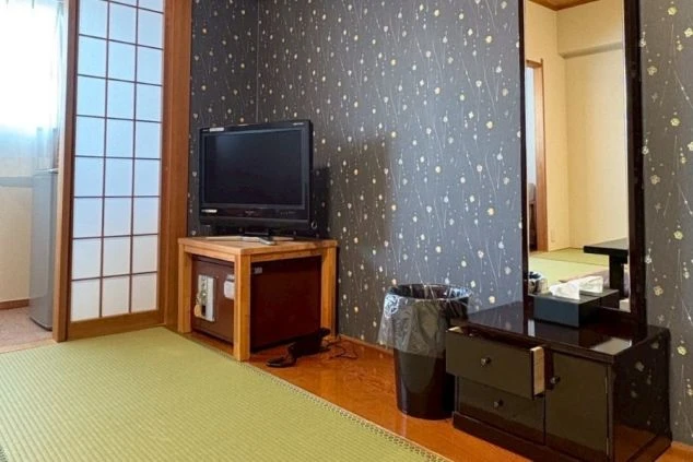 リゾートバイトの客室寮の和室の部屋の画像。黒いドレッサーとテレビ、ゴミ箱が置かれ、奥には和室が広がっている。リゾートバイトの寮の部屋の画像。