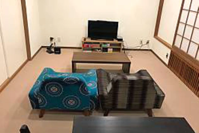 リゾートバイトの寮のリビングスペース。ローテーブルと2つの低いソファが置かれ、テレビを見ながらくつろげる空間になっている。