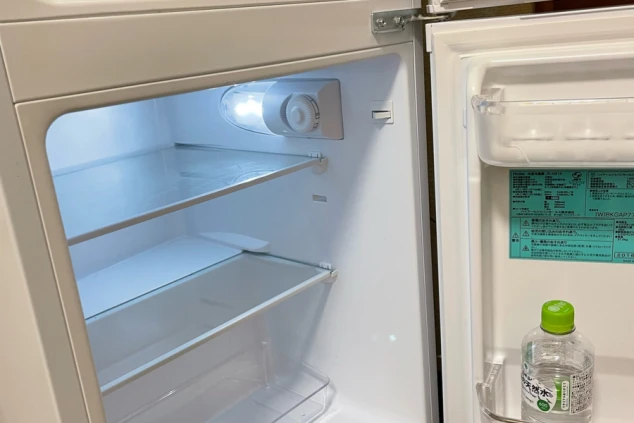 リゾートバイトの個室寮に備え付けられた小型冷蔵庫。庫内はきれいに整理されており、自炊や飲み物の保存に便利な設備の画像。
