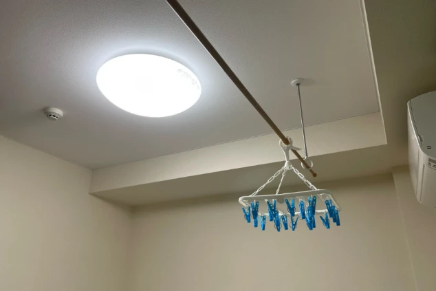 リゾートバイトの個室寮にある室内物干しと、天井の照明。雨の日でも洗濯物を干せる便利な設備の画像。