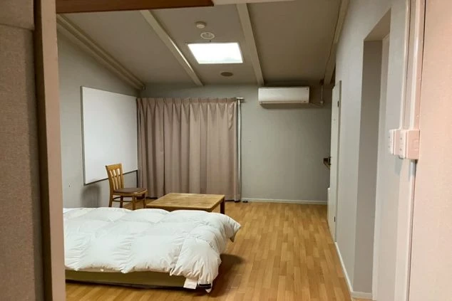 リゾートバイトの寮の個室。フローリングの床に布団が敷かれ、テーブルと椅子、エアコンが完備された、屋根裏部屋のような雰囲気のある部屋です。