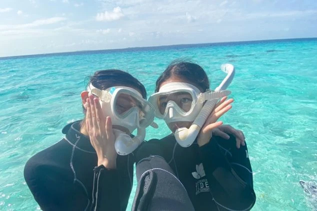 シュノーケルマスクとウェットスーツを着用した2人の女性が、透明度の高いエメラルドグリーンの海でポーズをとっている。沖縄や離島でのマリンアクティビティの仕事や、休日の過ごし方をアピール。