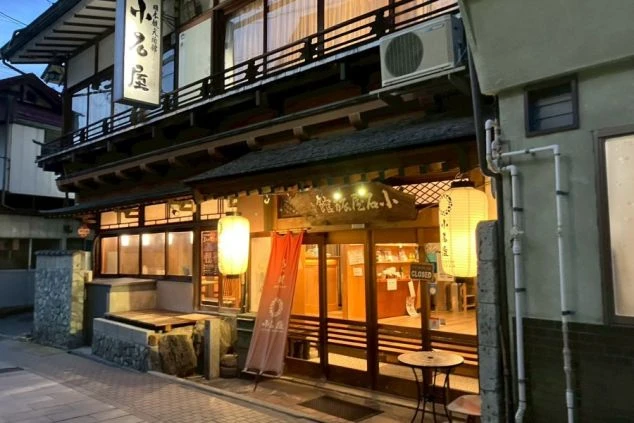 木造のレトロな建物で、正面には提灯や赤いのぼりが飾られ、窓からは暖かい光が漏れている。