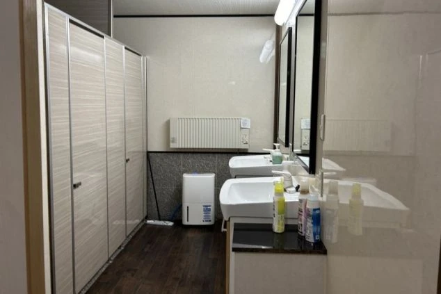 寮の洗面所。2つのシンク、鏡、暖房器具、個室トイレの扉が映る。