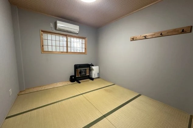 寮の和室。畳の床にエアコン、暖房器具、壁掛けコートハンガーが映る。