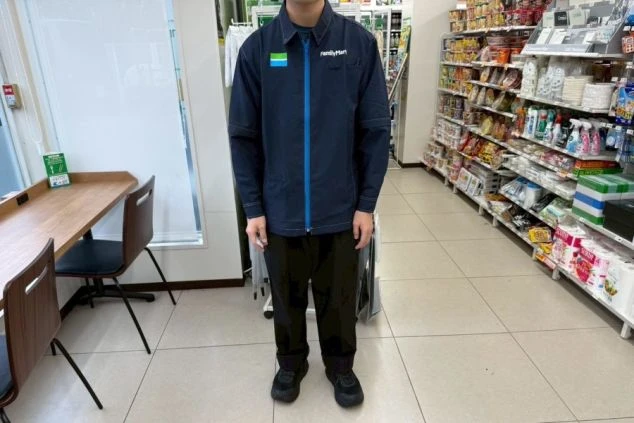 紺色のジップアップブルゾンと黒いズボンを着用した、コンビニスタッフの制服姿。