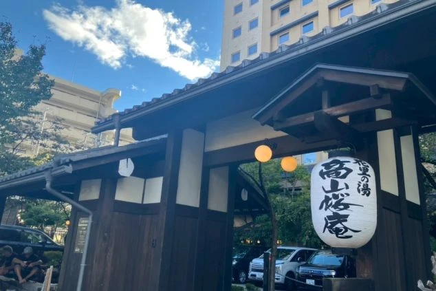 「高山桜庵」と書かれた大きな提灯が吊り下げられた、木造の立派な門構え。奥には高層の建物が見える。