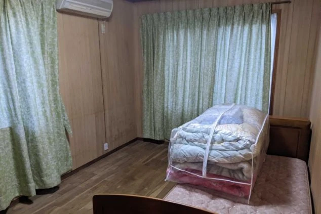 リゾートバイトの社員寮の部屋を表現するイメージ画像。ベッドやエアコン、カーテンが備え付けられたシンプルな個室。