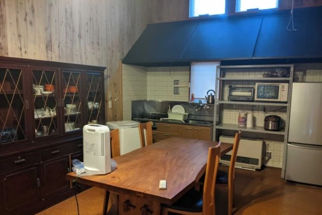 リゾートバイトの社員寮にある共用キッチンのイメージ画像。木製のダイニングテーブルや棚、冷蔵庫が設置されている。