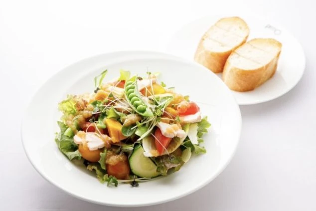 軽井沢のレストランで提供される料理の例。チキンや新鮮な野菜が入った色鮮やかなサラダと、添えられたバゲットが写っている。