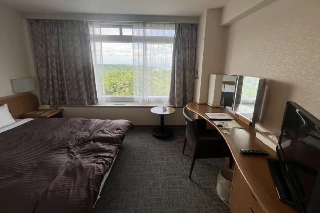 リゾートバイトの寮の部屋の中を撮影した画像。部屋にはベッド、デスク、ドレッサーが備え付けられており、窓からは豊かな自然が見える。リゾートバイトの寮の部屋の画像。