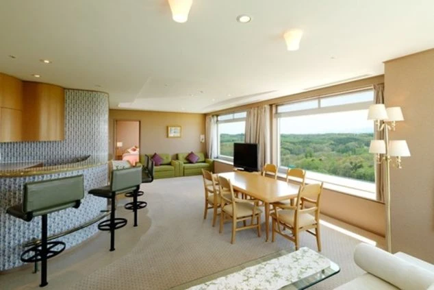 窓の外に緑豊かな自然が広がる、広々としたリビングの画像。ダイニングテーブルやソファ、そしてカウンターキッチンが備え付けられている。リゾートバイトの寮やホテルの共有スペースの画像。