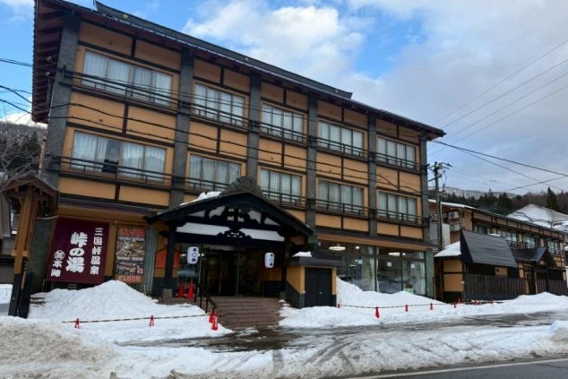 雪が積もる街道沿いに佇む、伝統的な和風建築の旅館外観。冬のリゾートバイトならではの、風情ある仕事環境のイメージ。