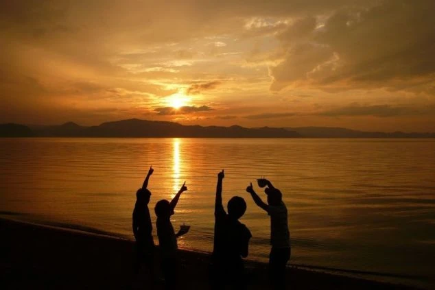4人のシルエットが、夕日の沈む湖畔で手を上げてポーズをとっている画像。リゾートバイトを通じてできた友人たちと、夕日を眺めて楽しんでいる様子が伝わってくる画像の画像。