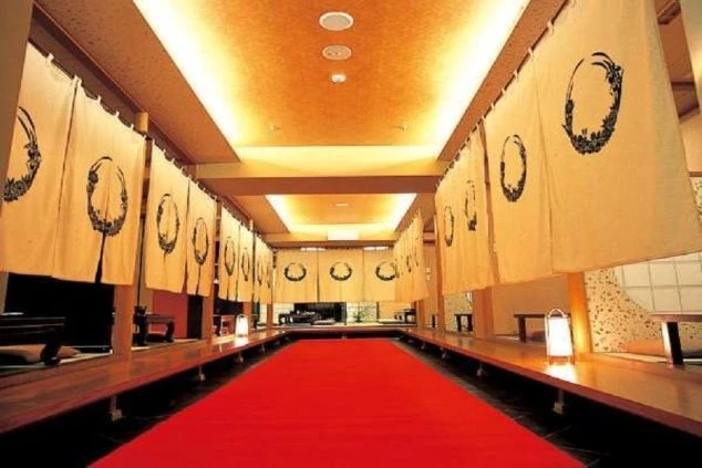 和風の落ち着いた雰囲気の食事処の画像。中央には赤い絨毯（じゅうたん）が敷かれ、両脇には暖簾（のれん）がかけられた個室が並んでいる。リゾートバイトの仕事内容を表す、ホテルのダイニングの画像。