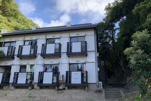 リゾートバイトの寮の外観の画像。2階建ての建物にはたくさんの窓とベランダがあり、裏には階段が設置されている。リゾートバイトの寮の外観の画像。