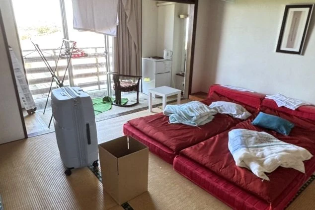 リゾートバイトの個室寮の室内。赤いマットレスと布団が敷かれた和室で、バルコニー、ミニ冷蔵庫、スーツケースが見える、住み込み生活の雰囲気が伝わる画像。