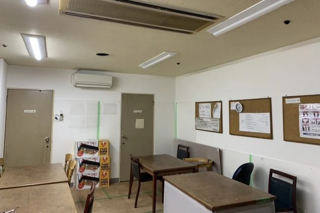 リゾートバイトの寮の共用スペースの画像。複数のテーブルと椅子が置かれており、掲示板が設置されている。リゾートバイトの休憩時間や食事の時間を過ごす、従業員食堂の画像。