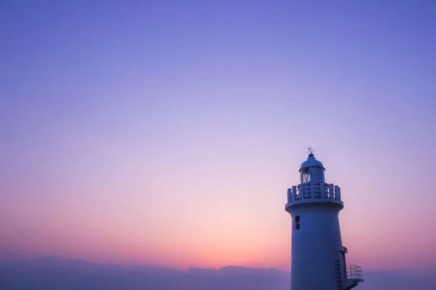 夕暮れの空を背景に、白い灯台がそびえ立っている画像。空はピンク色と紫色が混ざり合い、幻想的な雰囲気を醸し出している。リゾートバイトの休日に観光を楽しめる、風景の画像。