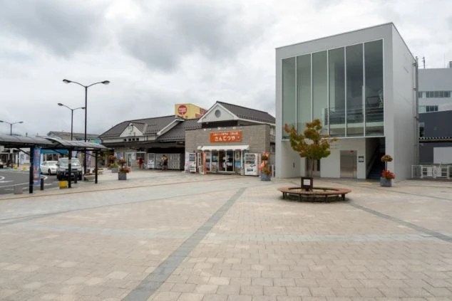 レトロな木造の駅舎と、モダンなガラス張りの建物が並んでいる。リゾートバイトの勤務地として、風情ある温泉地の玄関口をアピールする画像。