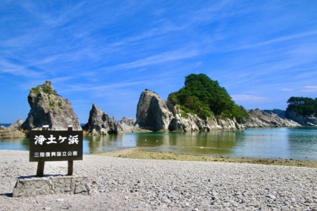 岩手県宮古市にある浄土ヶ浜の風景。「浄土ヶ浜」と書かれた看板と、海に浮かぶ奇岩が見える。白い砂浜と澄んだ水が、リゾートバイトの休日に訪れたい美しいビーチをアピール。