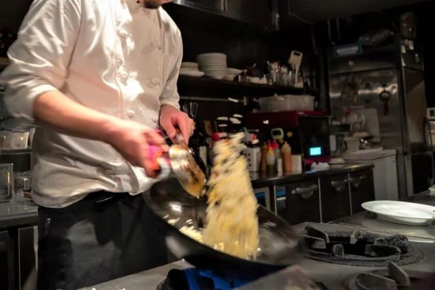 ホテルやレストランの厨房。調理師が炒め物をする風景。リゾートバイトの調理補助の仕事。