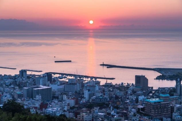夕焼けに染まる海と港町。オレンジ色に輝く海面に太陽の光が反射し、美しい景観を創り出している。リゾートバイトの休日に、幻想的な景色を堪能できることをアピール。