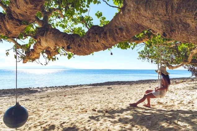  沖縄の断崖絶壁から見下ろす、エメラルドグリーンに輝く海と白い砂浜。壮大なスケールの景色が、リゾートバイトの休日に感動的な体験を与えてくれる。