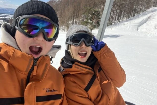 スキー場のリフトに乗っている2人組が、楽しそうに笑顔で写っている画像。