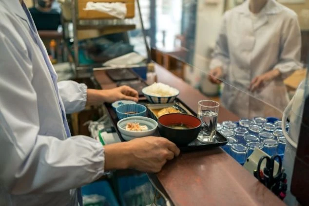 従業員が食事のトレーを準備している画像。レストランや食堂での調理業務をイメージ。