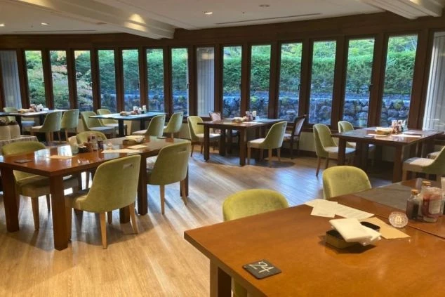 大きな窓から豊かな自然が見える、ホテルのレストランのダイニングの画像。たくさんのテーブルと椅子が並び、落ち着いた雰囲気で食事ができる。リゾートバイトの仕事内容を表す、ホテルのダイニングの画像。