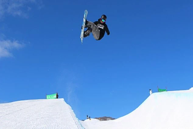 晴天のスキーパークで、高くジャンプして技を決めるスノーボーダー。青空をバックに、ダイナミックなトリックを披露しています。