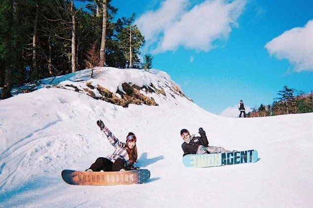 青空の下、雪の上に座ってポーズをとる男女2人が写っている画像。